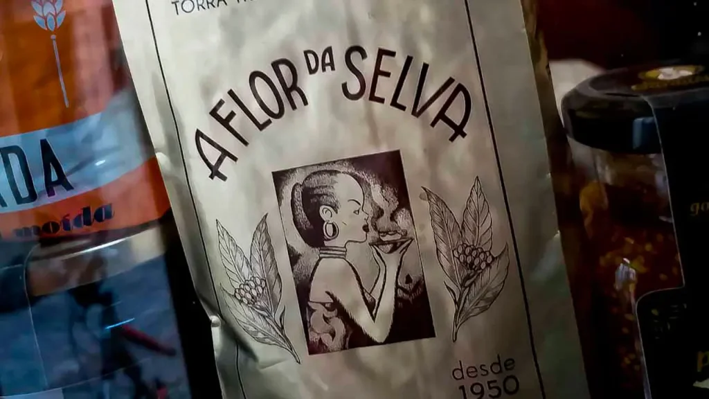 Imagem de marca da Torrefacção de Cafés Flor da Selva nos anos 50. É constituída por duas flores e uma figura feminina africana a apreciar uma chávena de café.