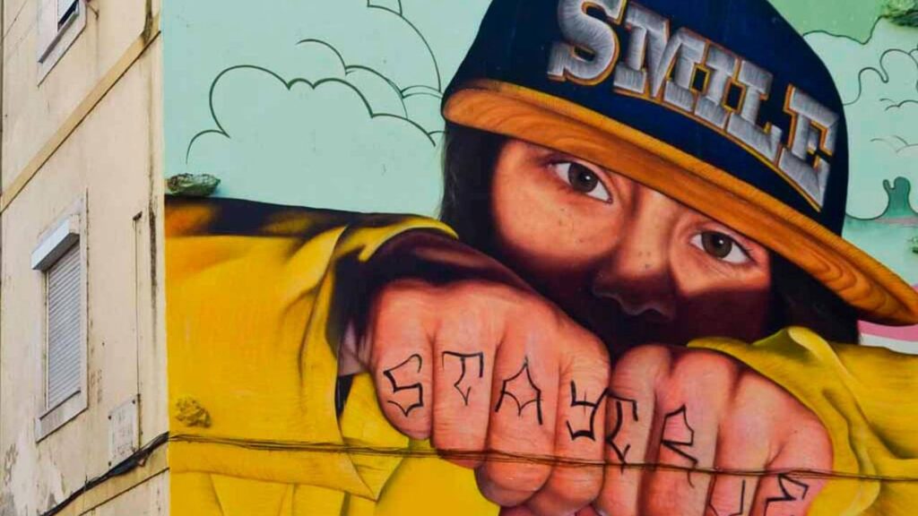 O Artista Urbano SMILE e o Fotorrealismo: mural de SMILE na Quinta do Cabrinha. Uma jovem que mostra os punhos fechados com a tatuagem “Stay True”.