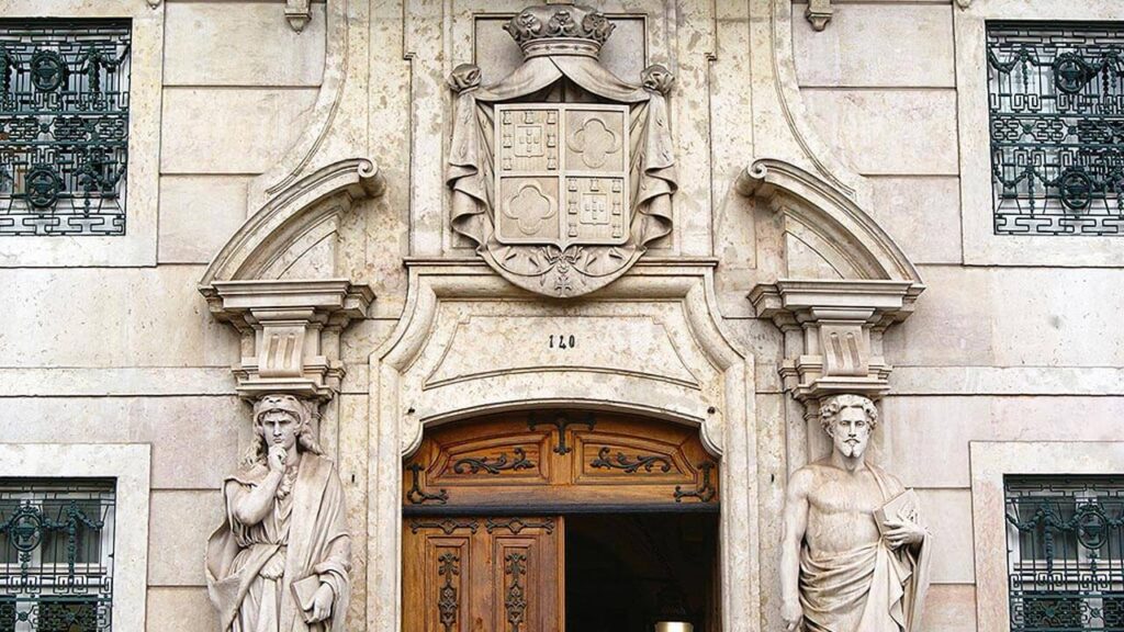 Portal principal do Palácio Palmela cuja moldura escultórica, coroada com o brasão dos Palmela, é ladeada por duas hermas que representam: à esquerda a Força Moral e à direita o Trabalho.